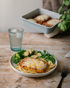 tofu parmigiana gratiné avec sauce tomate, fromage fondu et basilic frais, servi dans une assiette