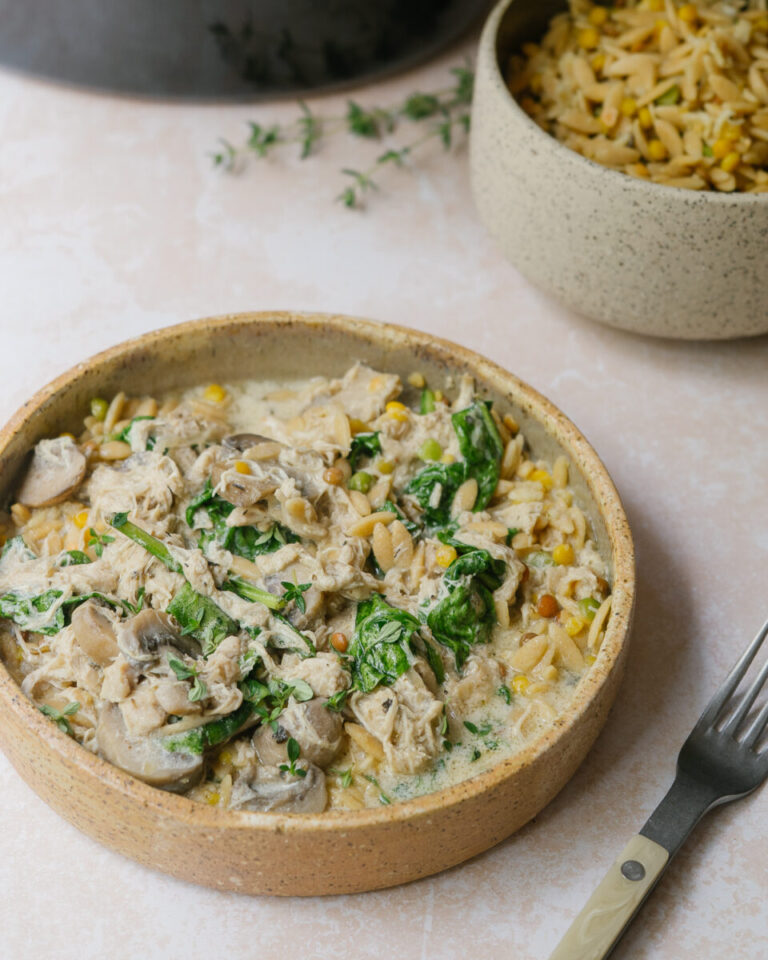 Poulet crémeux aux champignons à la mijoteuse servi sur de l'orzo avec une sauce onctueuse au parmesan et des épinards.