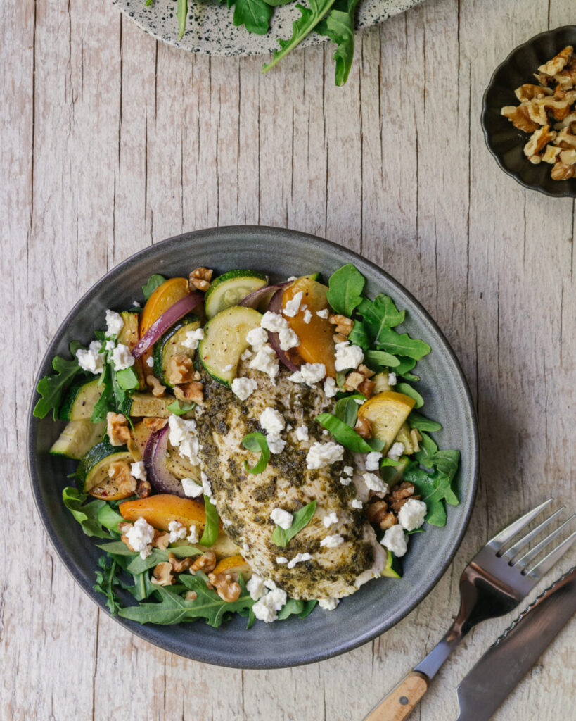 vue de dessus poulet au pesto sur la plaque avec courgettes et pêches grillées, servies dans un bol avec feta. recette de semaine facile sur la plaque
