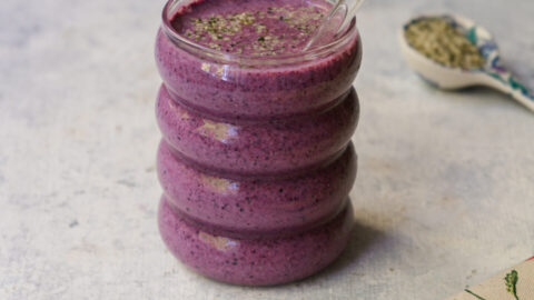 Smoothie aux bleuets et au citron garni de bleuets frais, de zeste de citron et de graines de chanvre dans un verre il goute le muffin aux bleuets