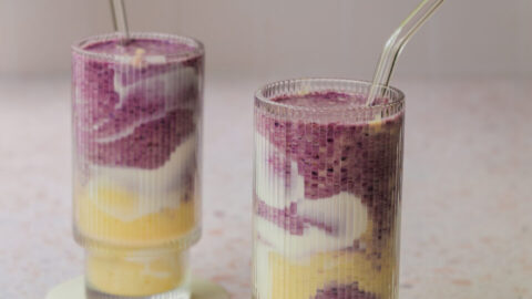 Smoothie marbré aux bleuets et à la mangue servi dans un verre, avec des tourbillons violets et orangés et une décoration de yogourt sur les parois.