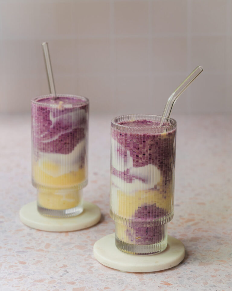 Smoothie marbré aux bleuets et à la mangue servi dans un verre, avec des tourbillons violets et orangés et une décoration de yogourt sur les parois.