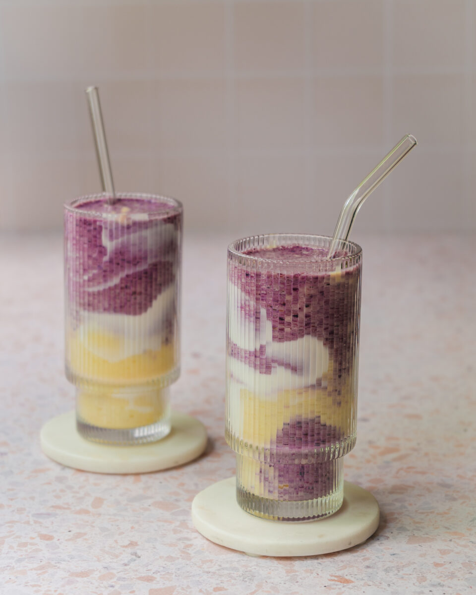 Smoothie marbré aux bleuets et à la mangue servi dans un verre, avec des tourbillons violets et orangés et une décoration de yogourt sur les parois.