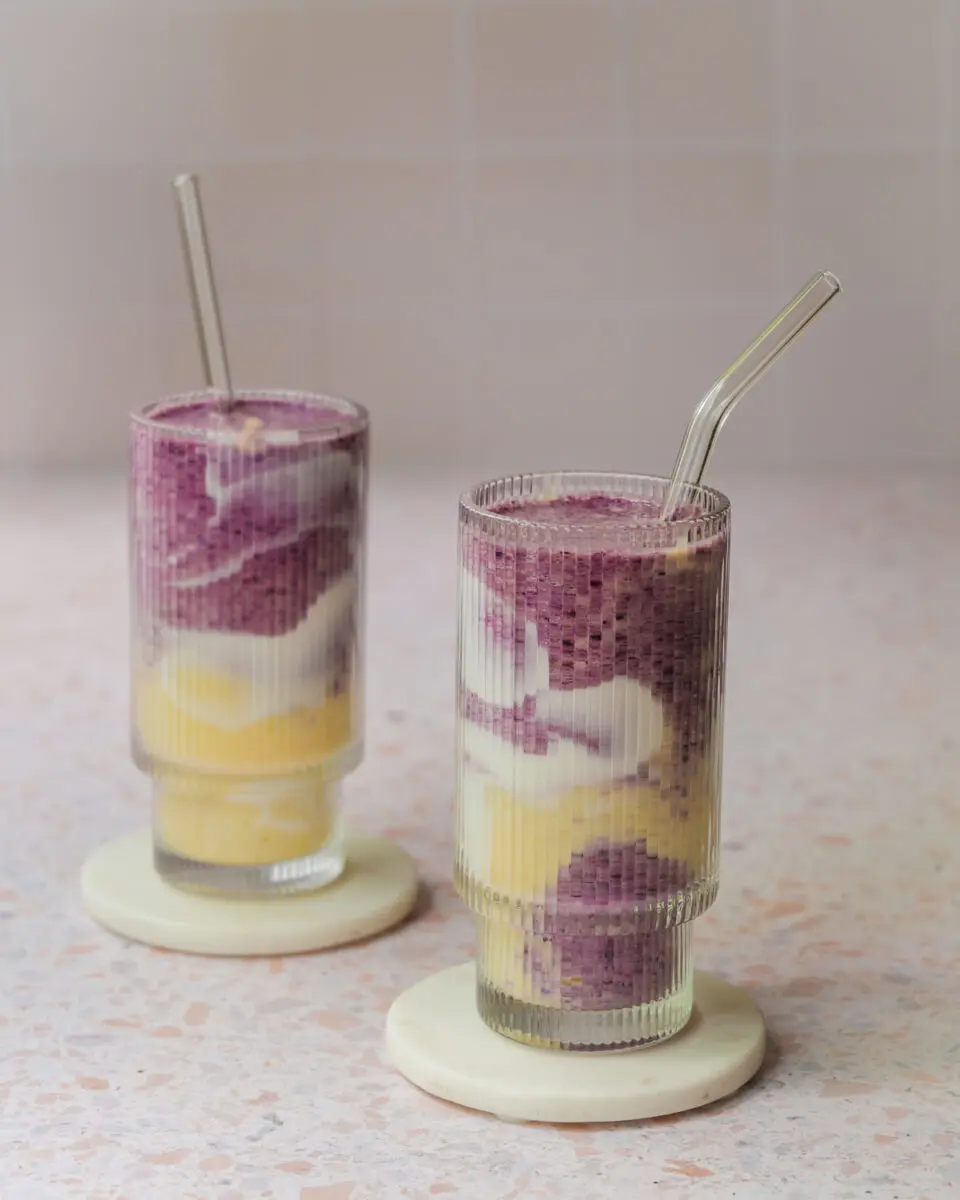 Smoothie marbré aux bleuets et à la mangue servi dans un verre, avec des tourbillons violets et orangés et une décoration de yogourt sur les parois.